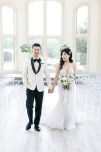 wedding couple at indoor wedding ceremony with ghost chairs