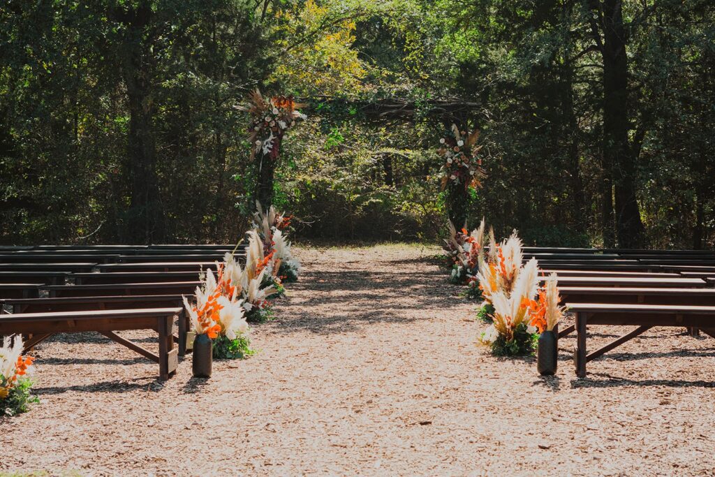 Outdoor wedding ceremony with wooden benches and boho floral arrangements lining the aisle