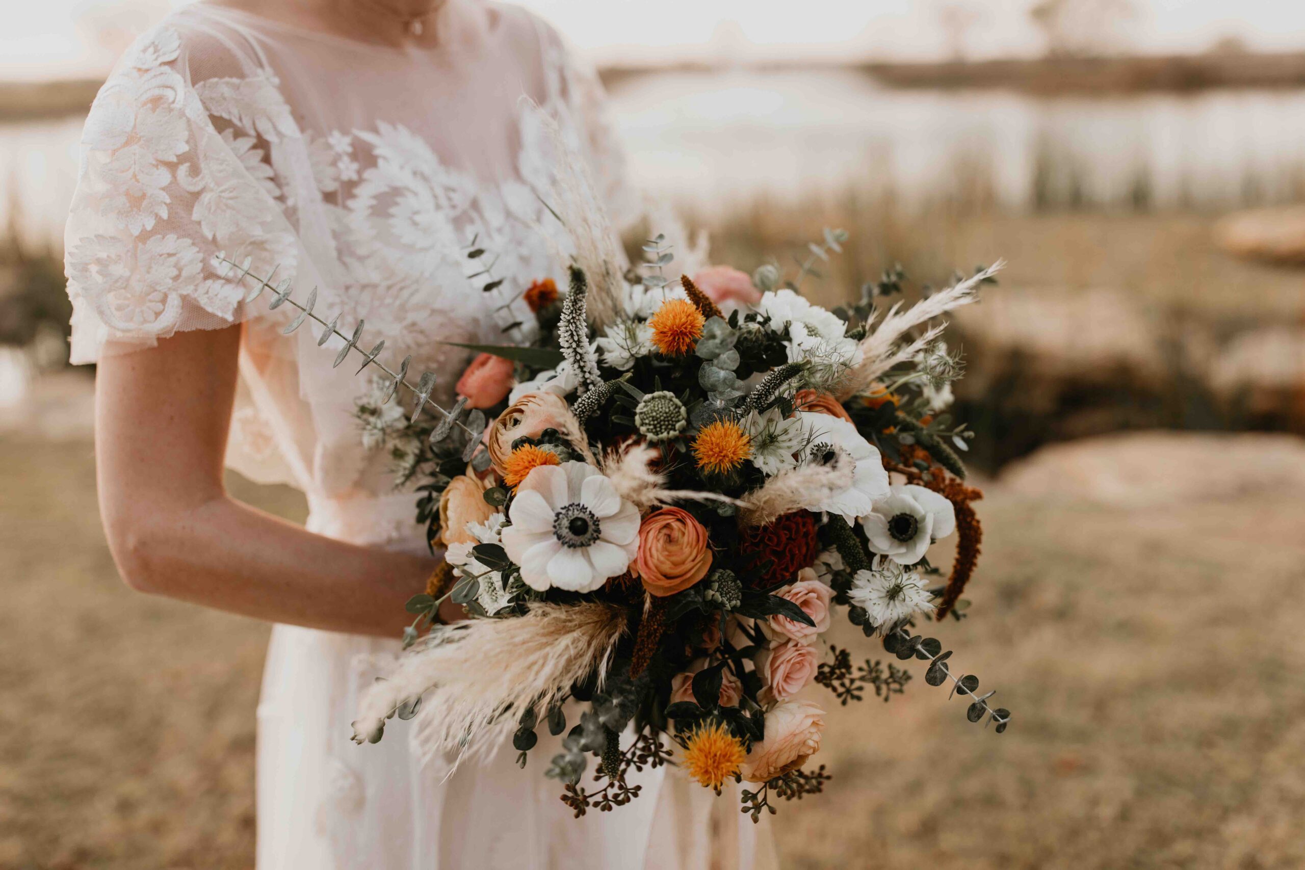 Bride holding fall bouquet featuring white, orange, and burgundy flowers