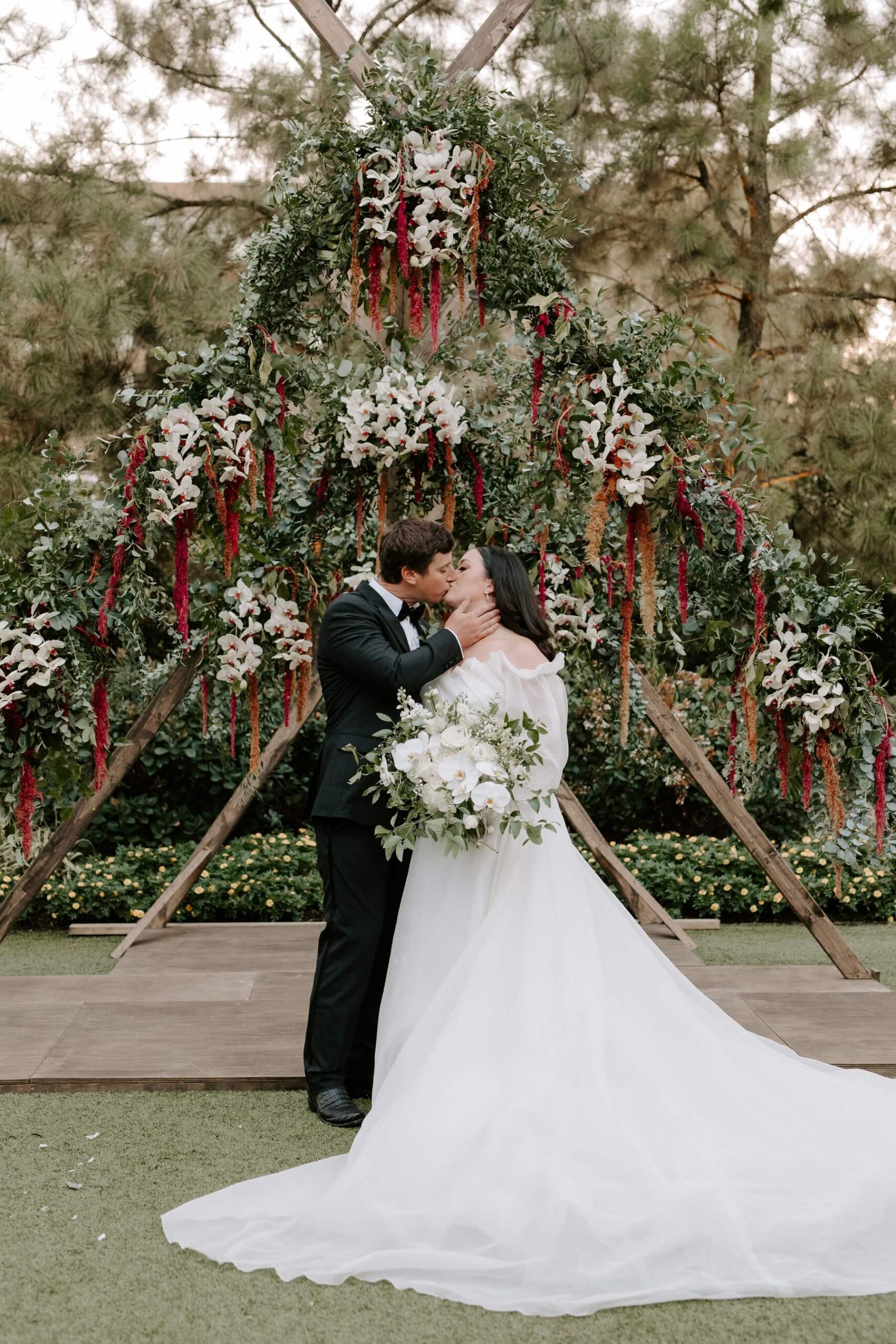 Bride and groom kissing under custom wedding arch adorned with hanging flowers