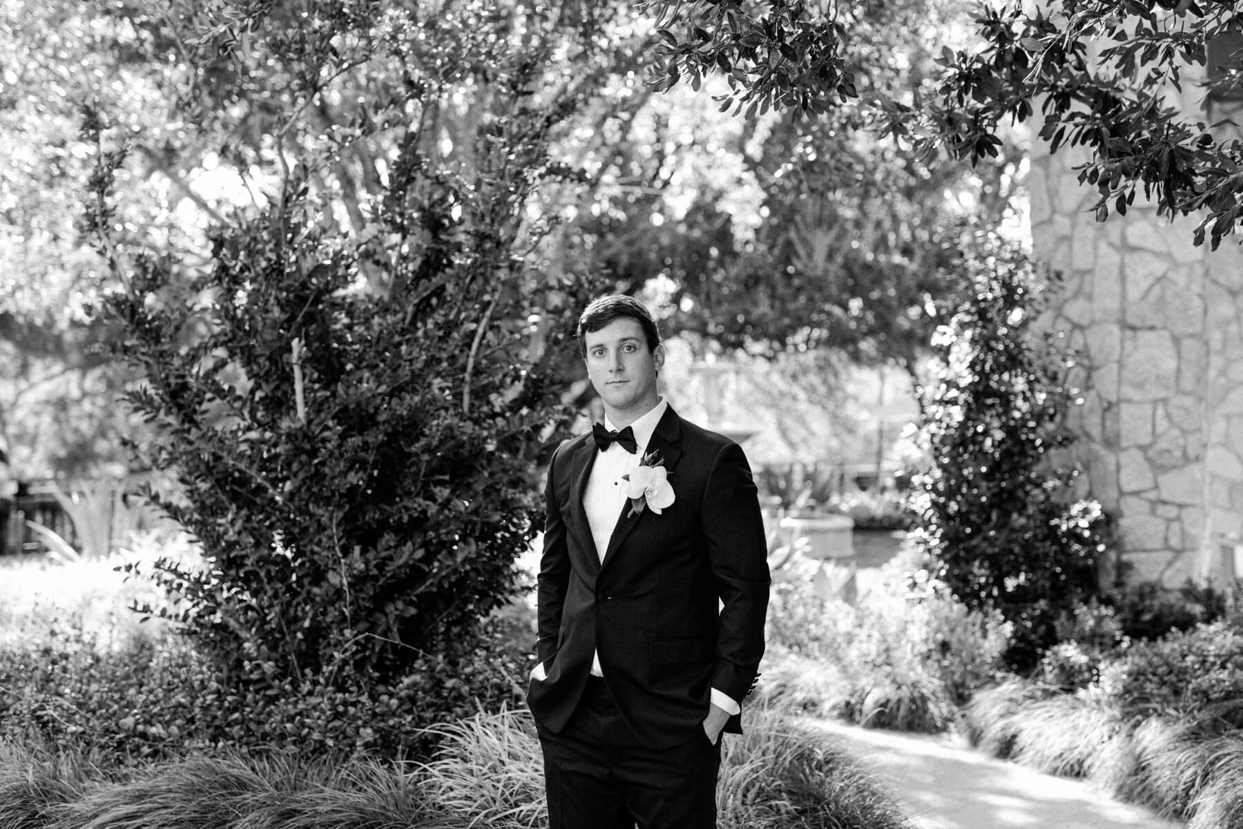 Groom in black suit with bowtie standing in Hotel Drover courtyard 