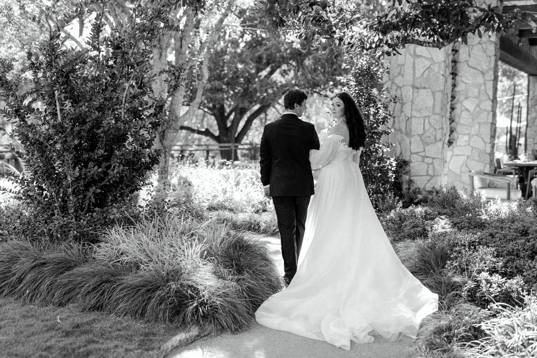 Bride looking over her shoulder as she and groom walk through courtyard 
