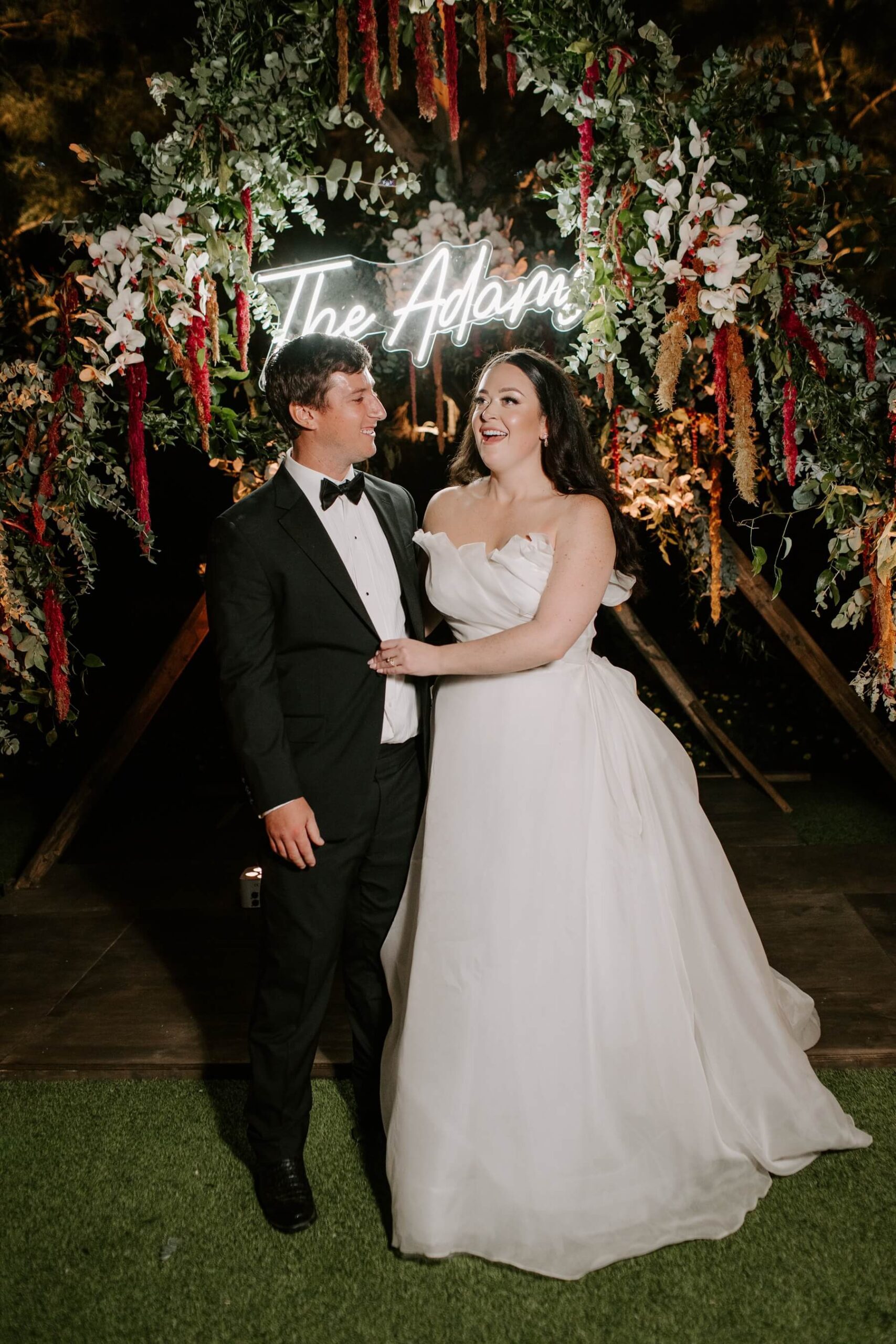 Bride and groom standing under custom altar with their last name in a neon sign