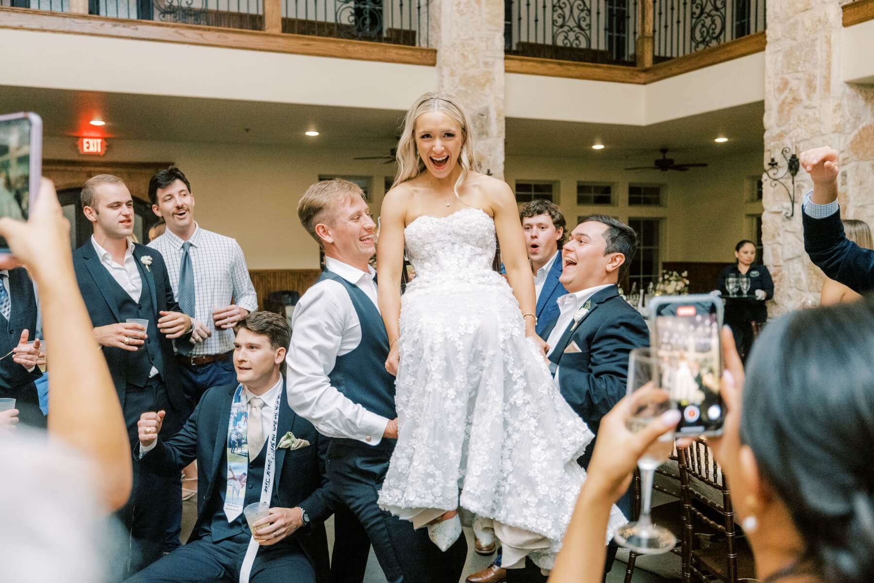 Bride being lifted on chair by groomsmen at wedding reception 
