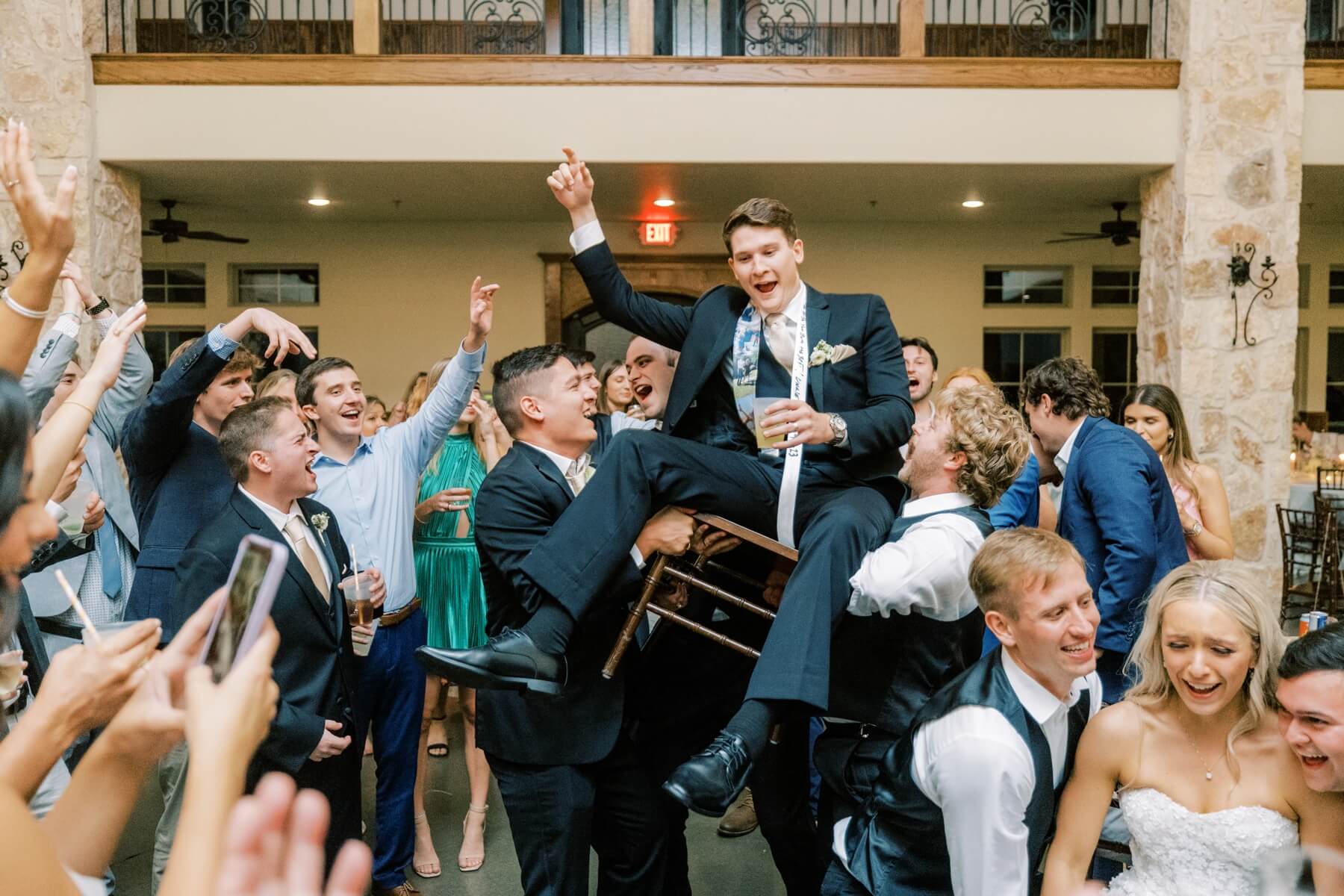 Groom being lifted on chair by groomsmen at wedding reception 