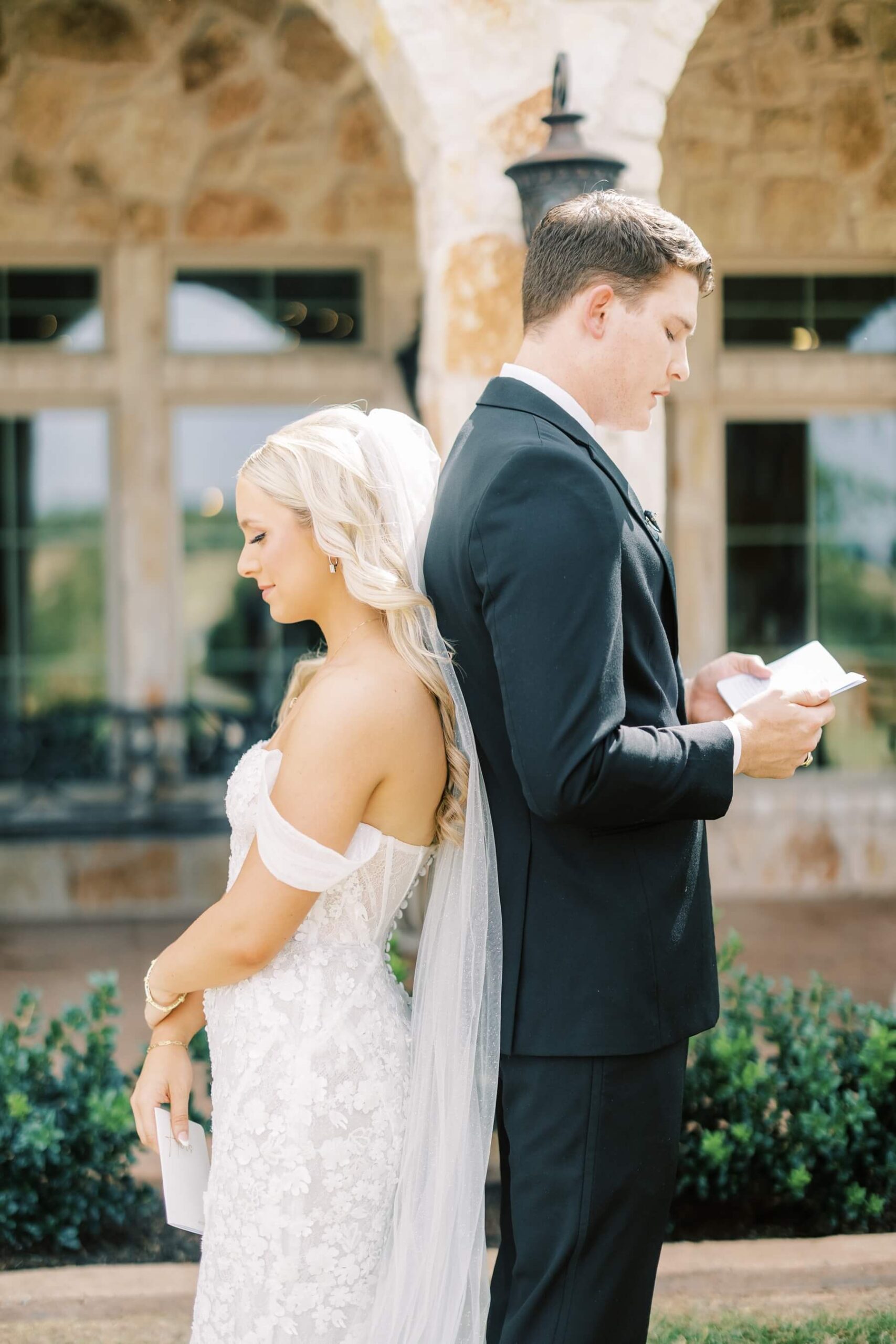 Bride and groom standing back to back reading private vows