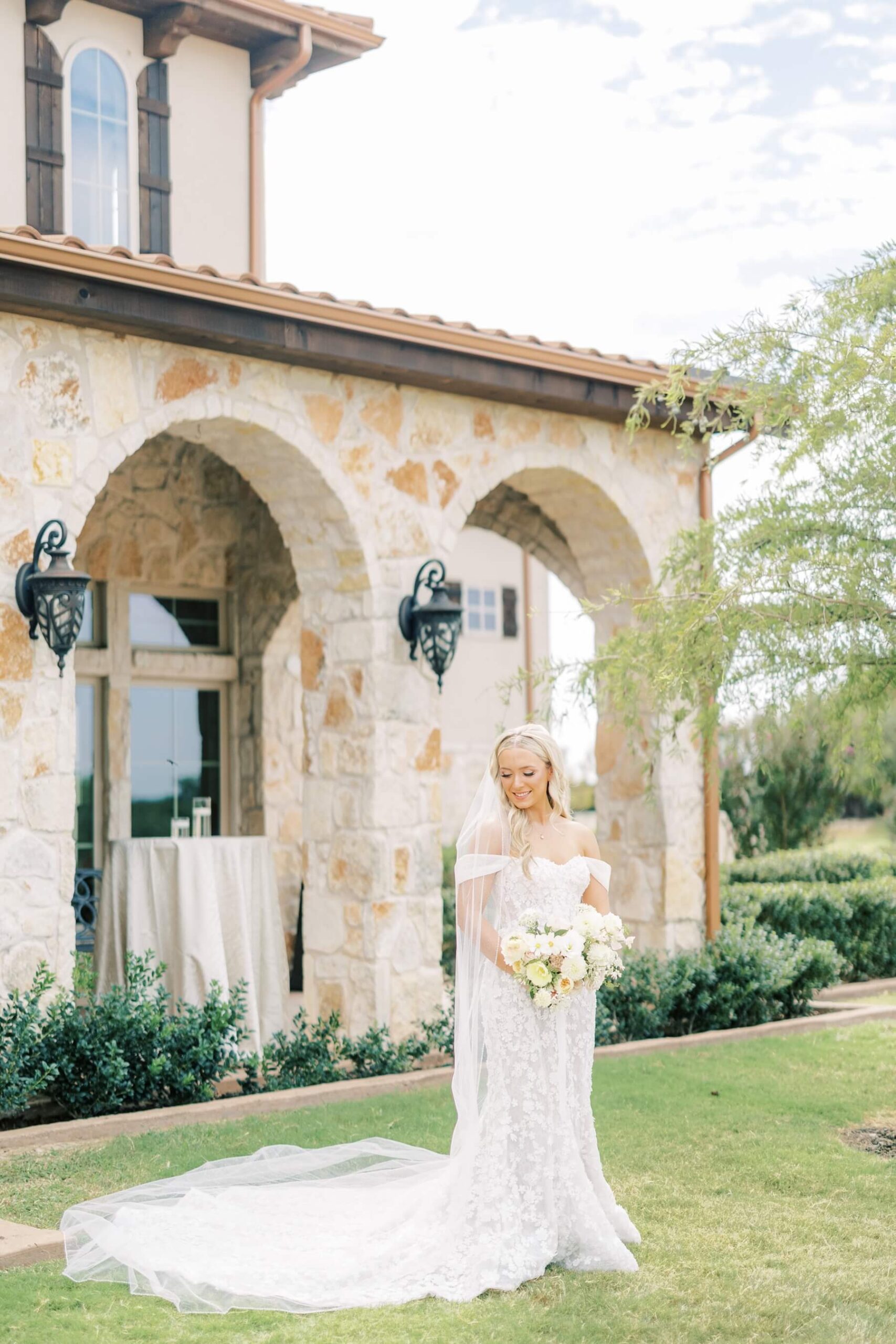 Bride wearing off the shoulder floral wedding dress standing in front of The Springs in McKinney