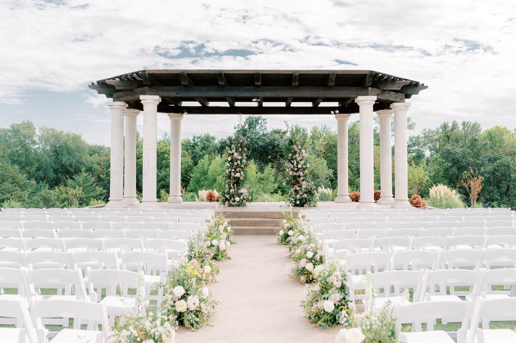 Ceremony space at The Springs in McKinney with floral arrangements lining the aisle and two floral towers at the altar