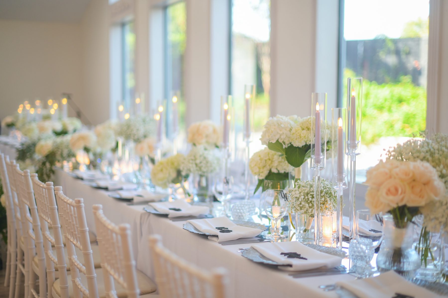 Reception table featuring white hydrangeas, white baby's breath, white candles, and white table linen at Brighton Abbey