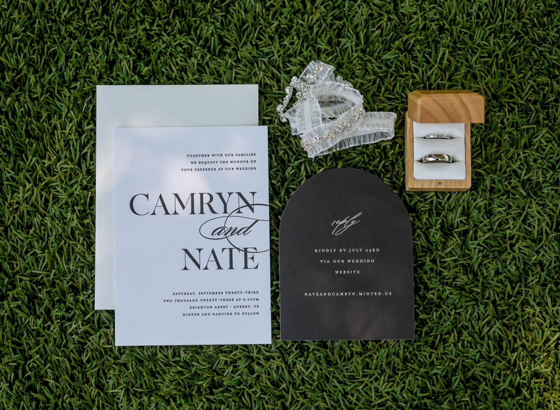 White and black wedding invitation with wedding rings and garter on green grass