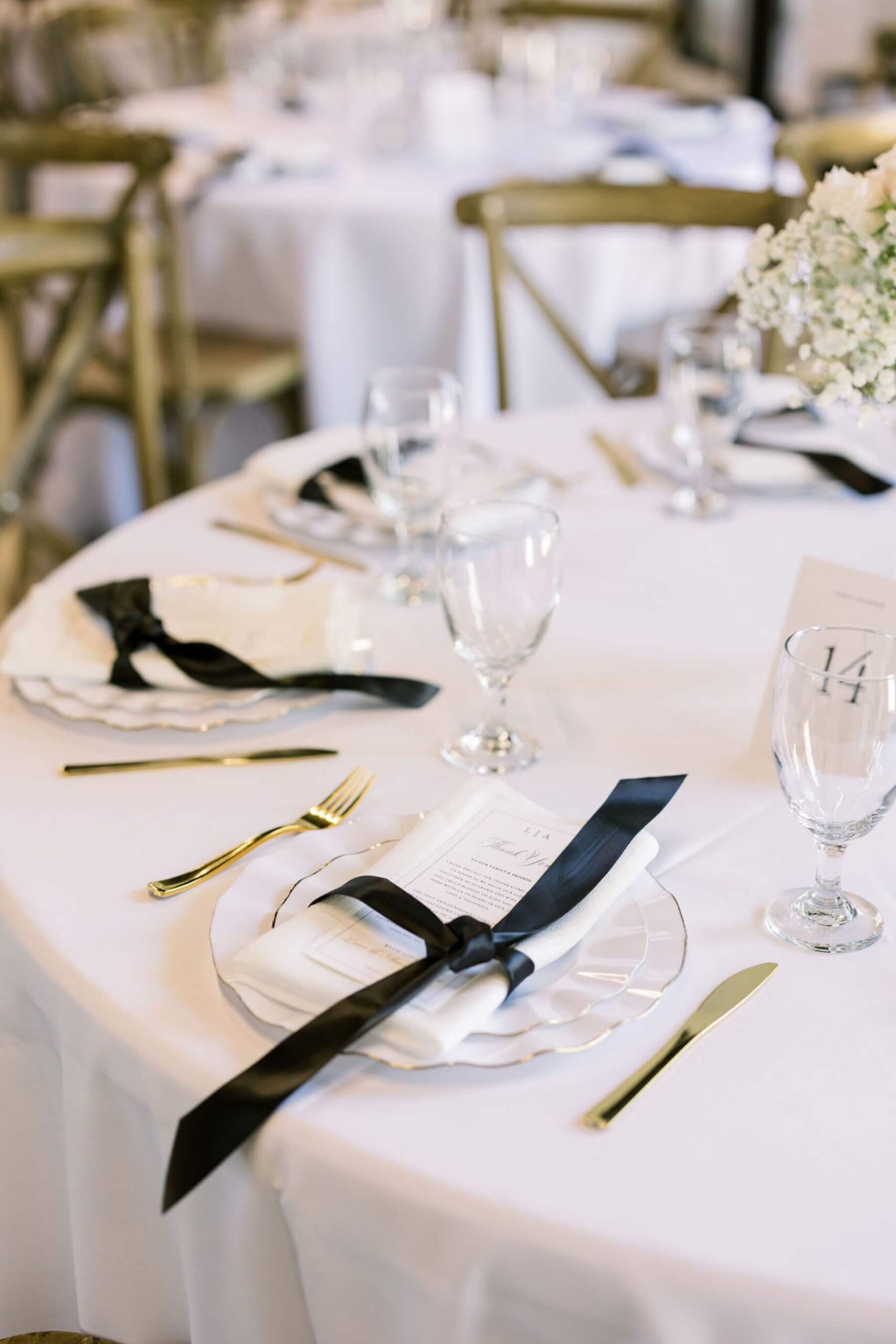Black and white wedding reception featuring white menus tied with black satin ribbon and white floral arrangements 