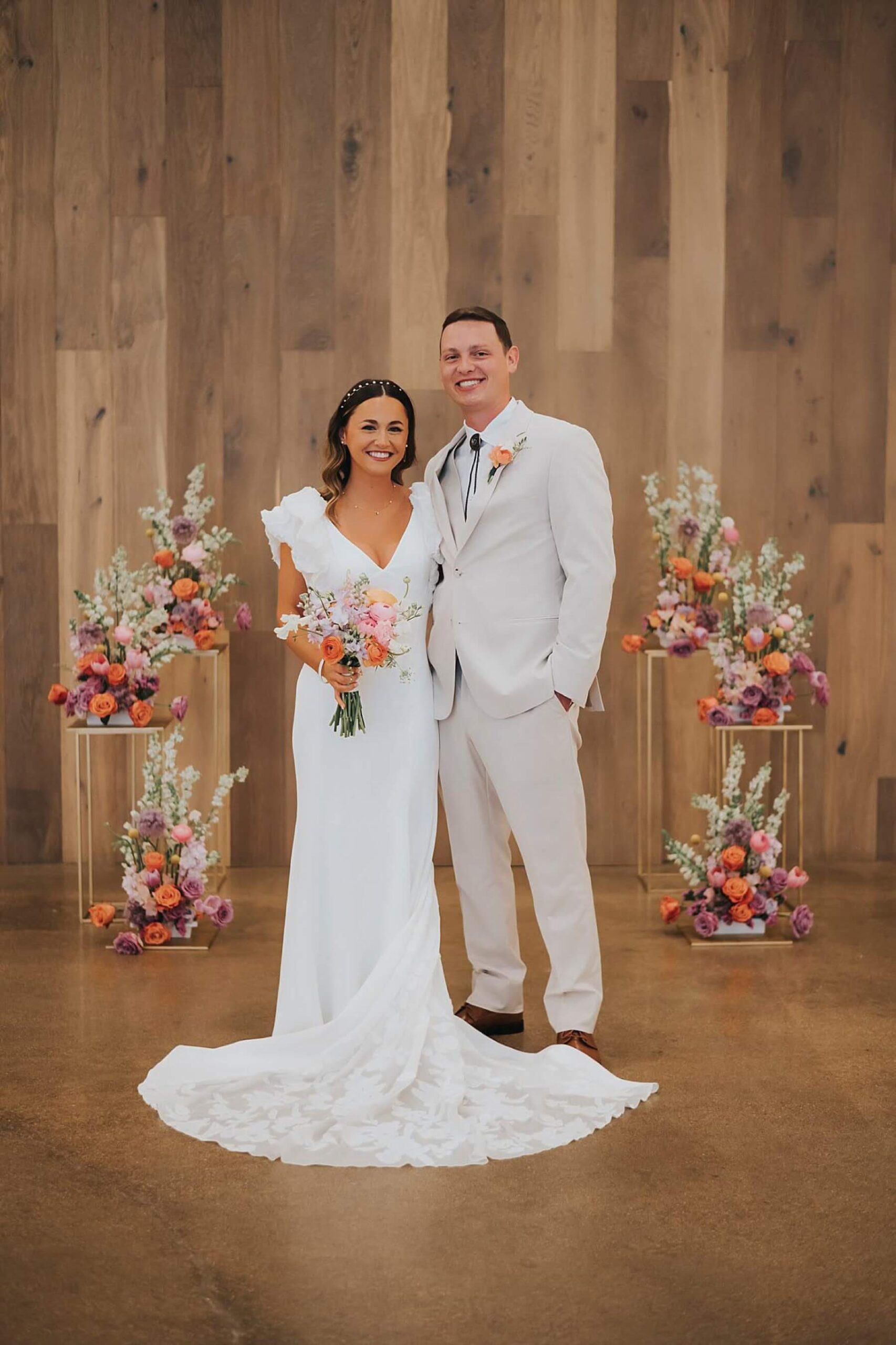 Bride and groom standing in front of ceremony florals featuring bright flowers 