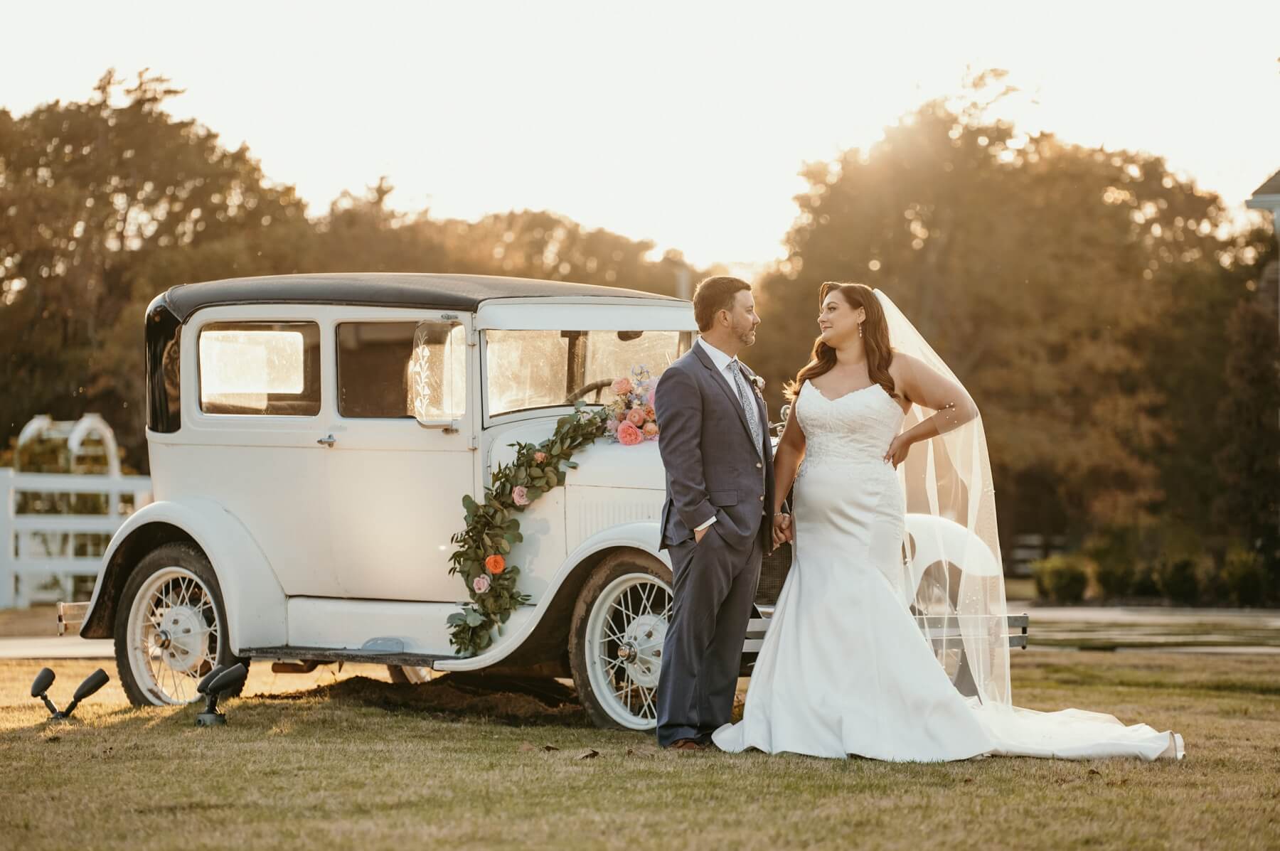Bride and groom looking at each other in front of vintage car