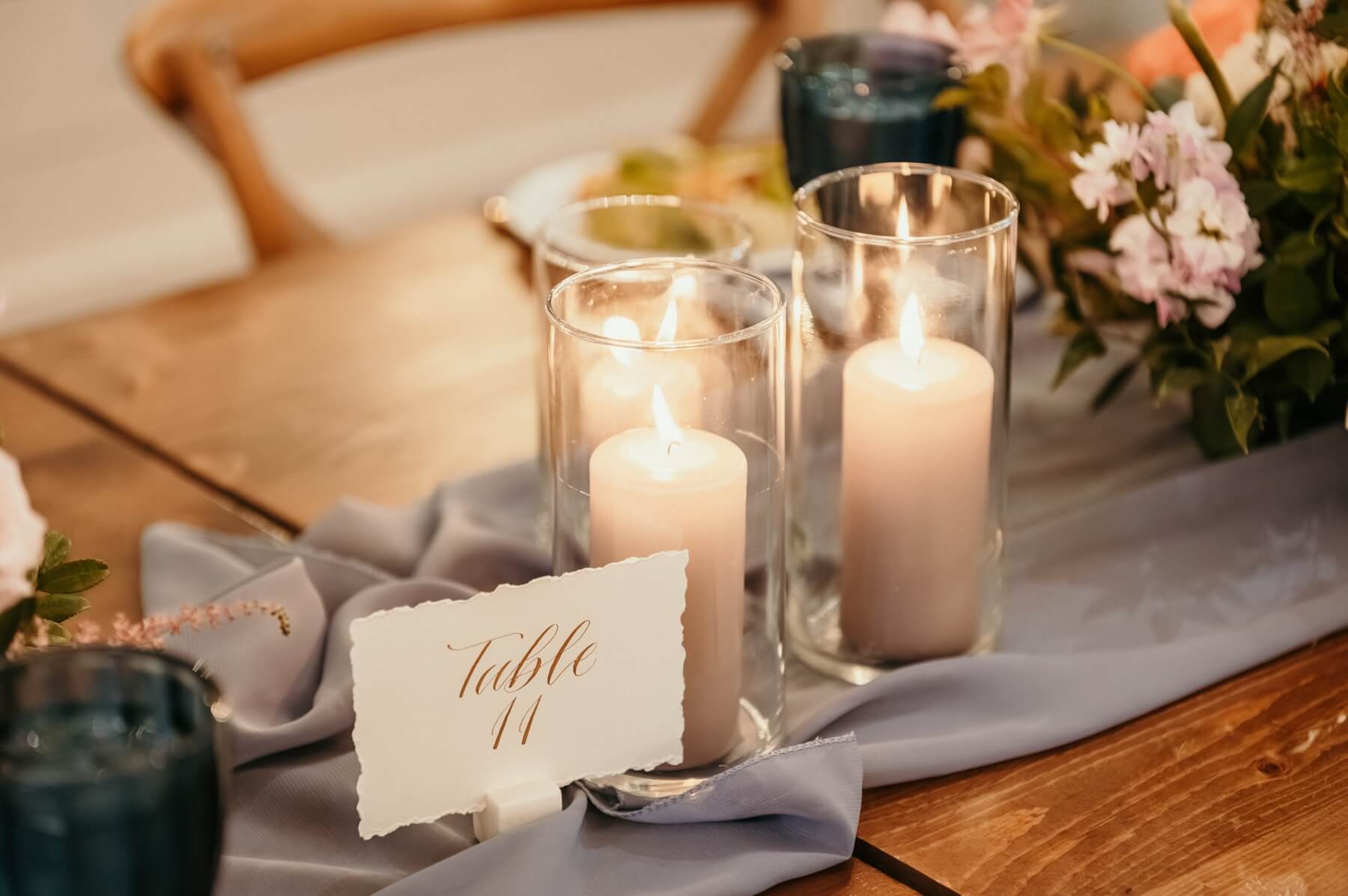 White candles on blue runner with white table number card