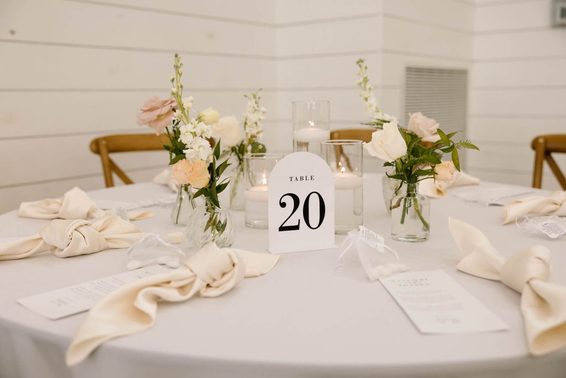 Reception decor including white napkins, flowers, candles, and table numbers