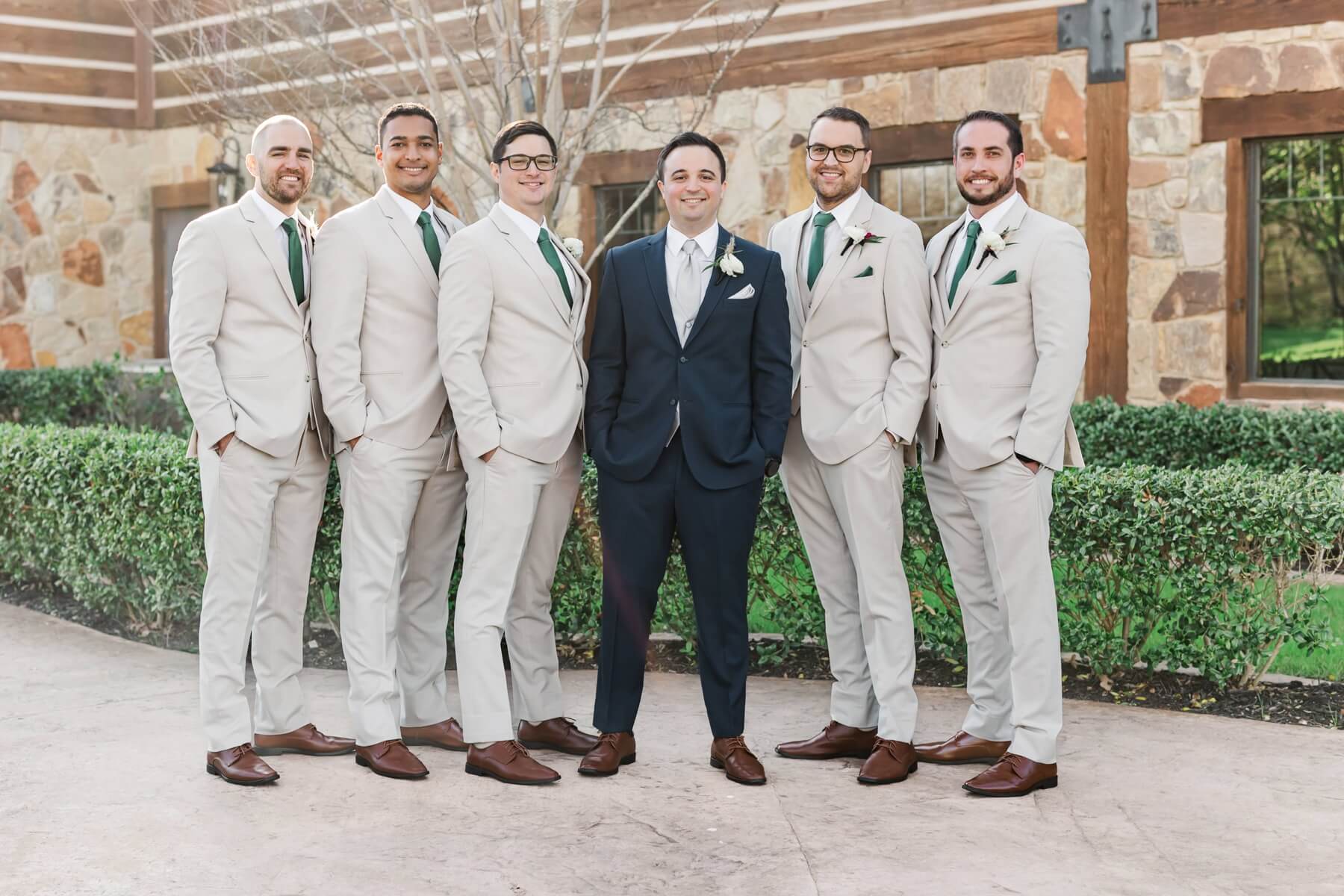 Groom wearing navy suit next to groomsmen in tan suits