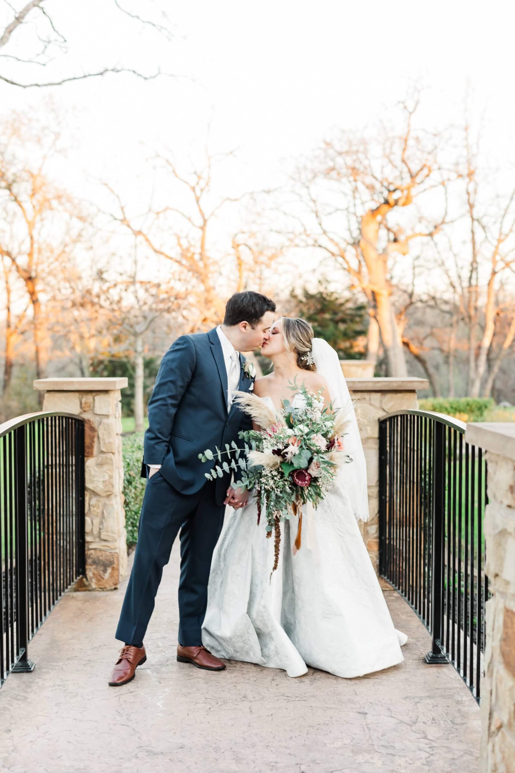 Bride and groom kissing on bridge at The Springs in Denton