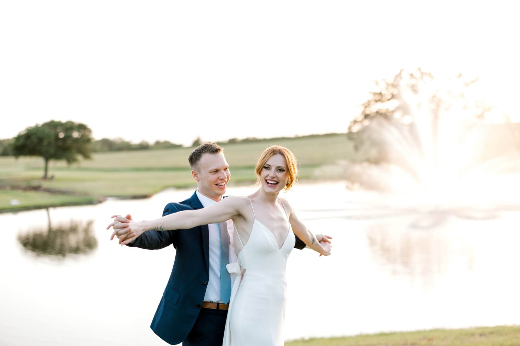 Bride and groom standing in front of pond during golden hour