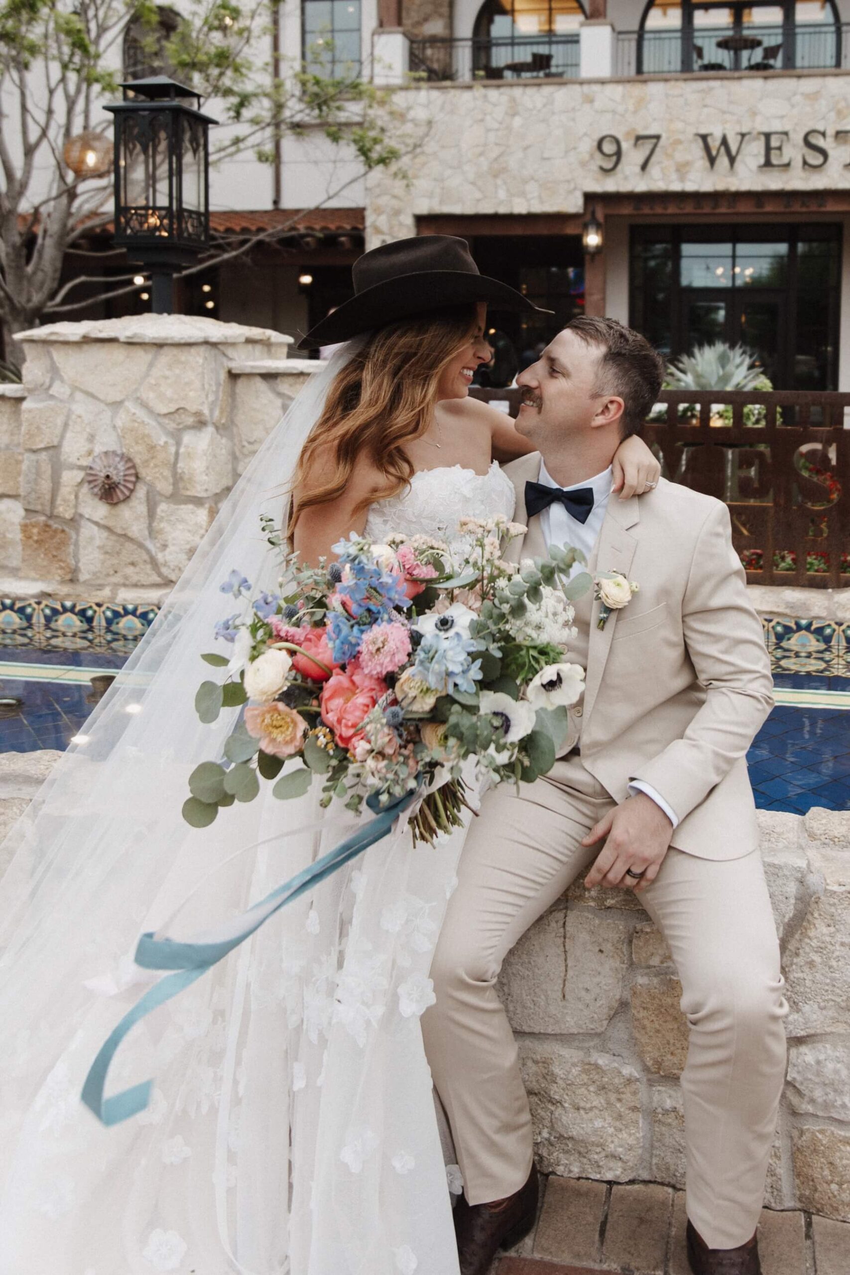 Bride wearing groom's cowboy hat while sitting on his lap