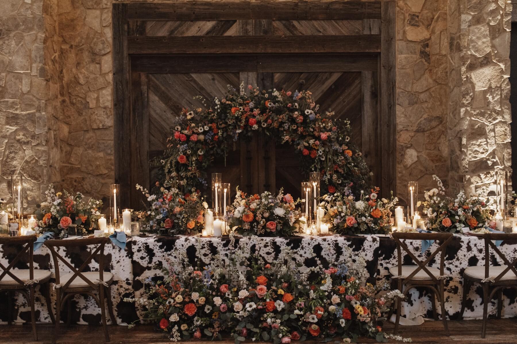 Head table with cowhide table cloth, colorful floral arrangements, and white candles